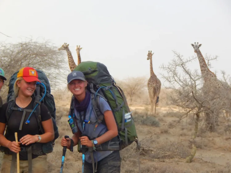 Students smile in front of giraffes while backpacking through Tanzania.