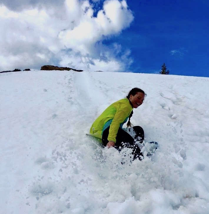 smiling person sleds down a hill in a spray of snow