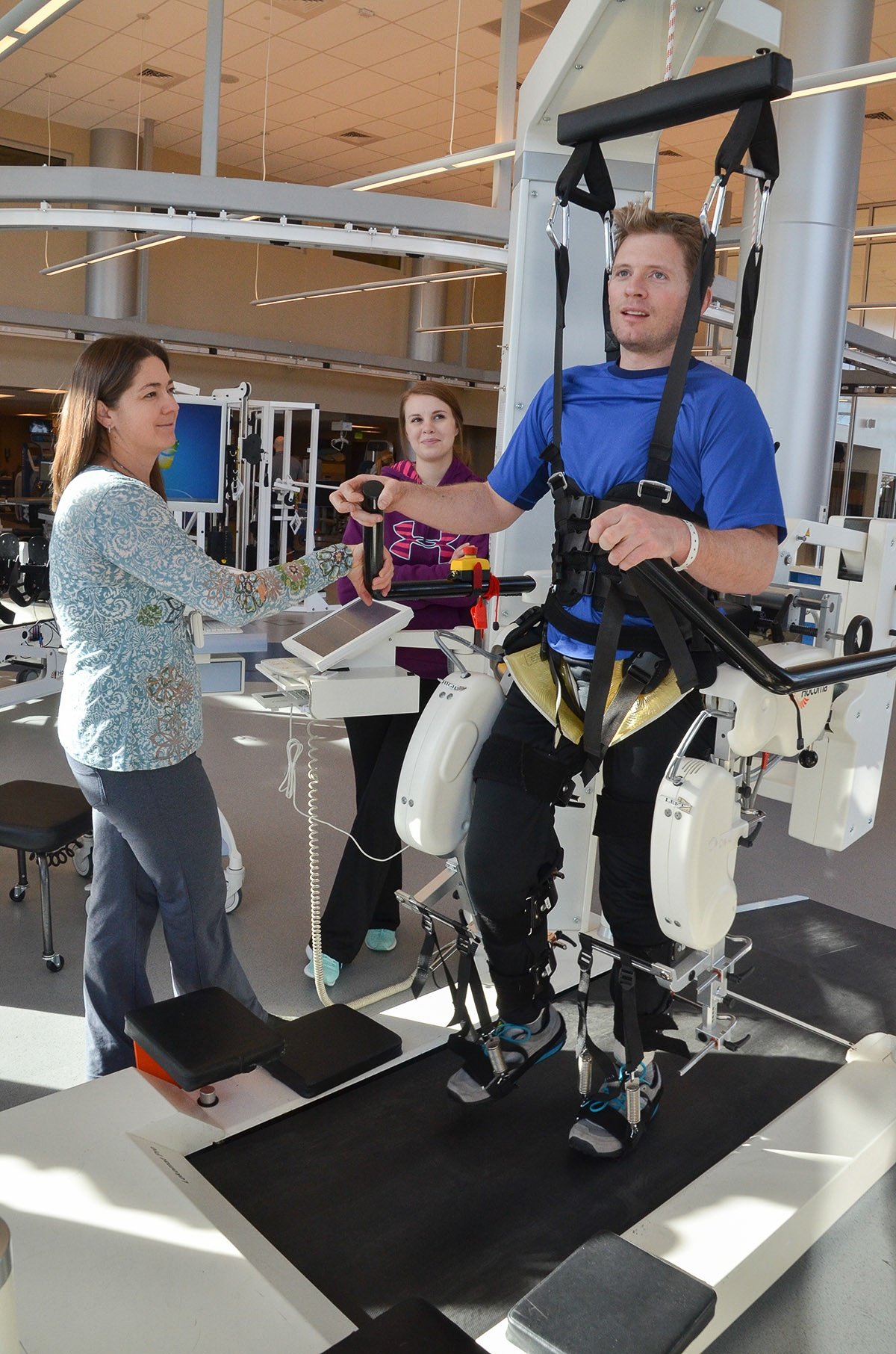 Jim Harris works with two physical therapists while strapped into an exercise machine