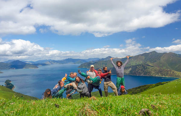 NOLS students pose for a group picture in New Zealand's mountains with blue water behind