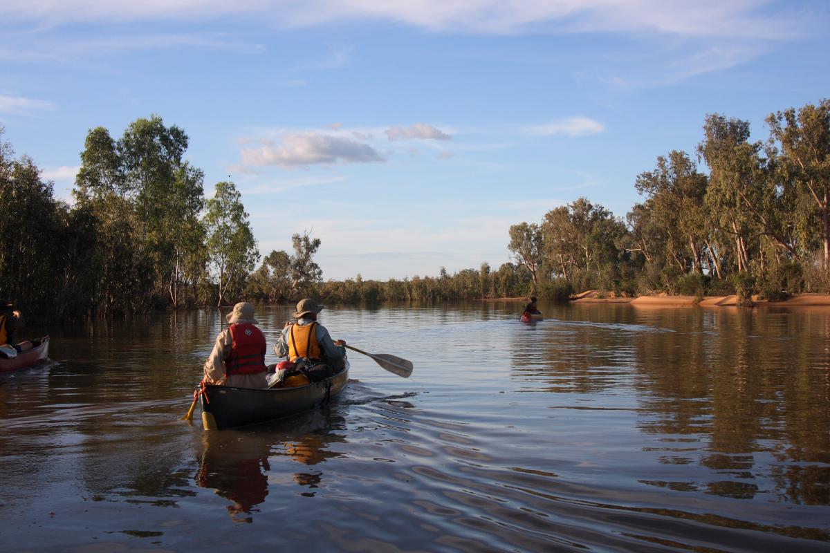Two people paddle a canoe down a calm waterway.