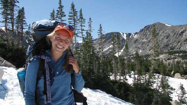 Eleanor Asma with pack with pines and snow-covered mountains