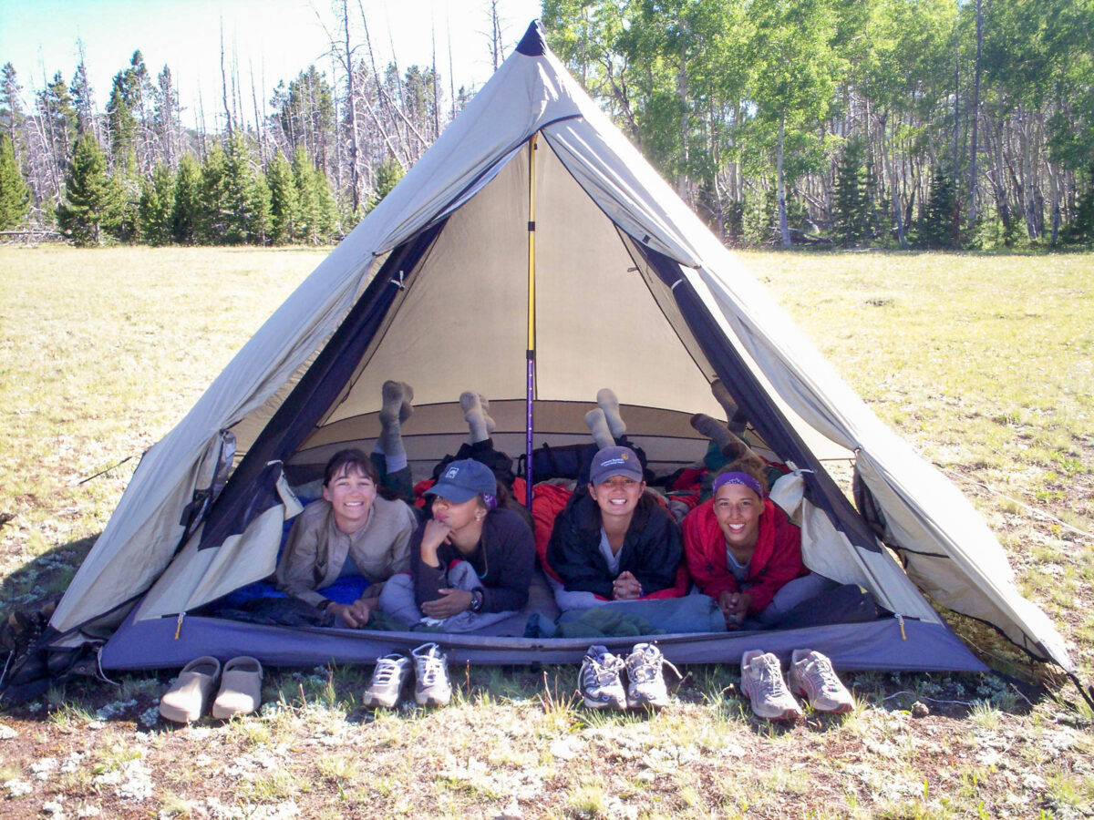 four teen girls racing the tent opening laying down looking at the camera with their shoes outside on the ground in front of them.