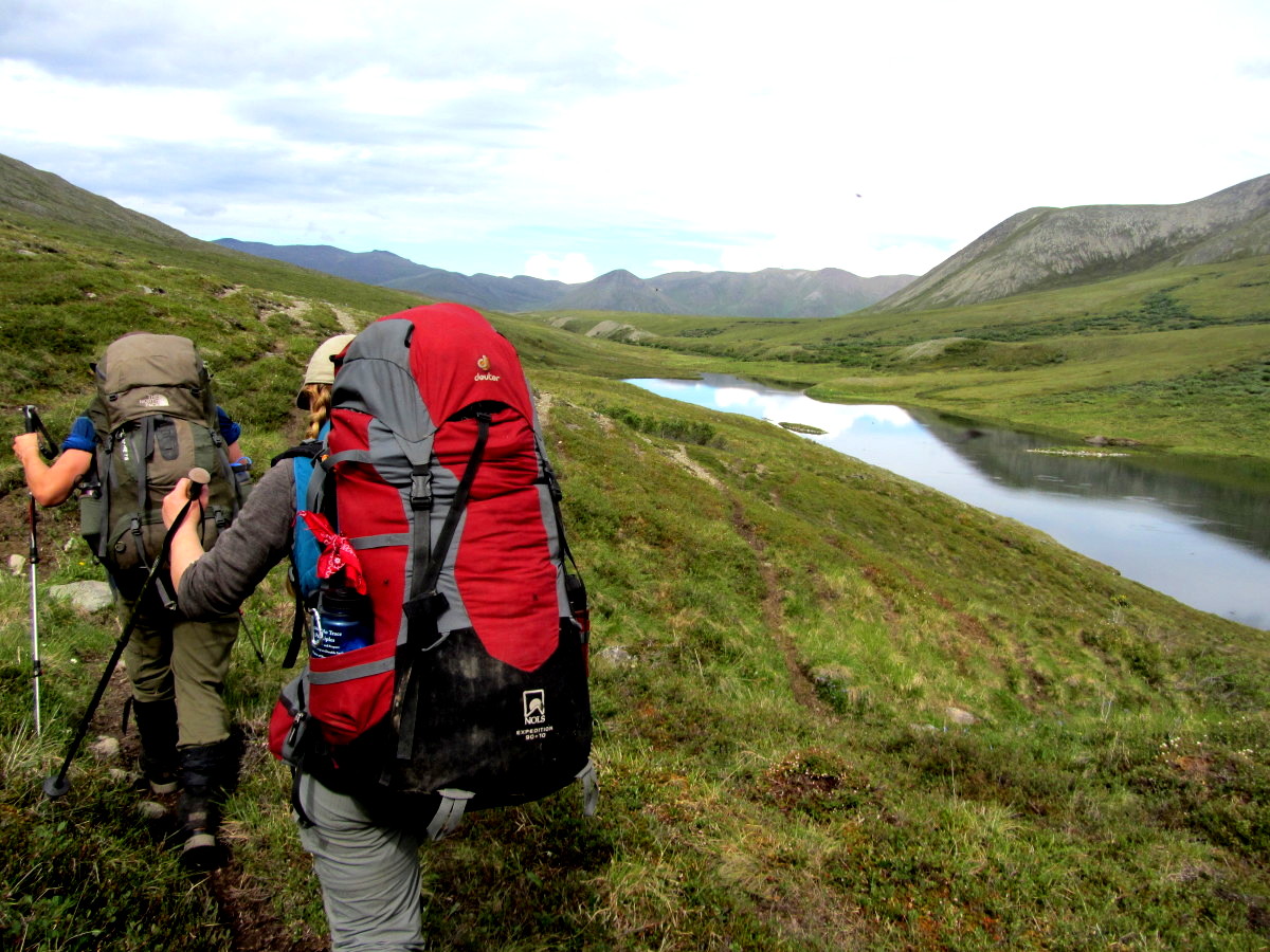 two women backpacking along a small pond through the backcountry