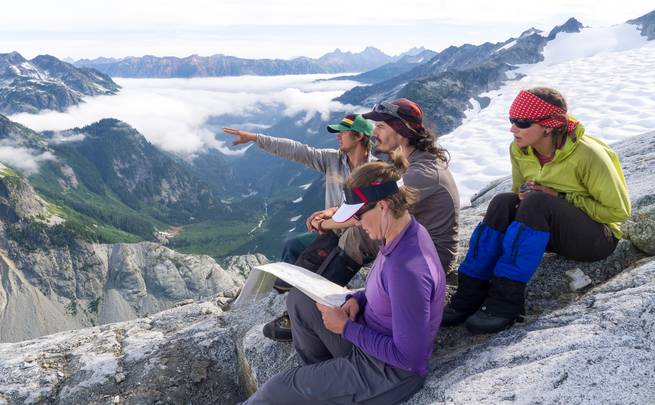 Trip leaders sitting on a rocky ridge above the clouds and gazing out at surrounding snowy peaks in the Pacific Northwest.