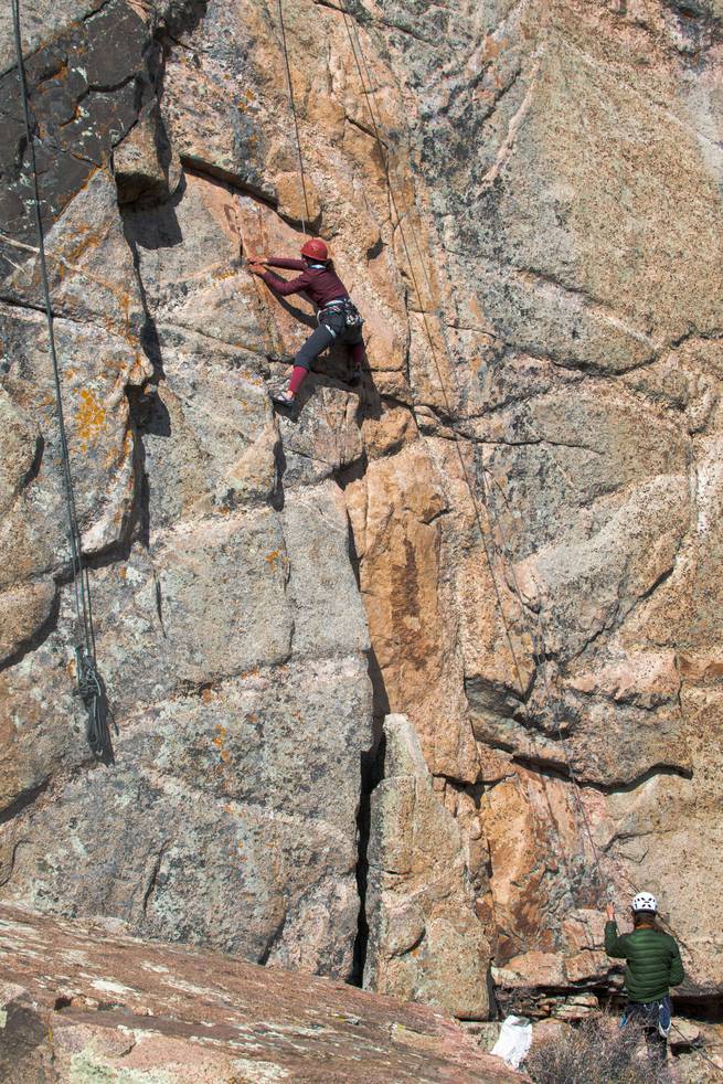 One student climbing a cliff face, while another is belaying.