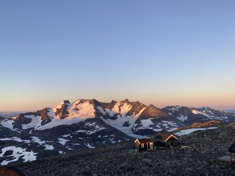An orange glow against a snowy peak. The sky above the mountain is dark, indicating it's sunset.