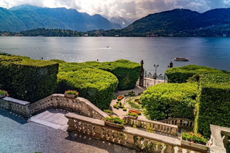 Well manicured gardens among a staircase lead down to the lake with the mountains framing the photo in the background.