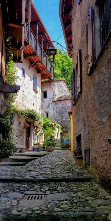A narrow alley surrounded by stone buildings and colorful vines and flowers.