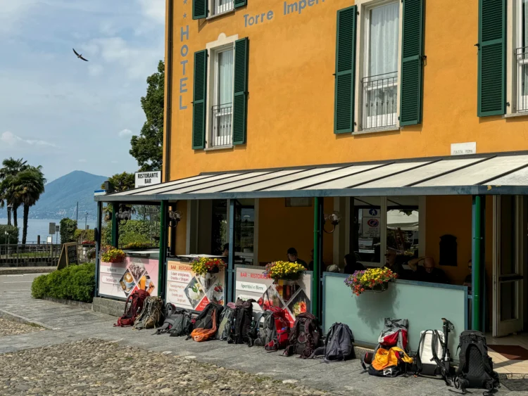 Colorful backpacks sit in front of a yellow hotel with the lake in the background.