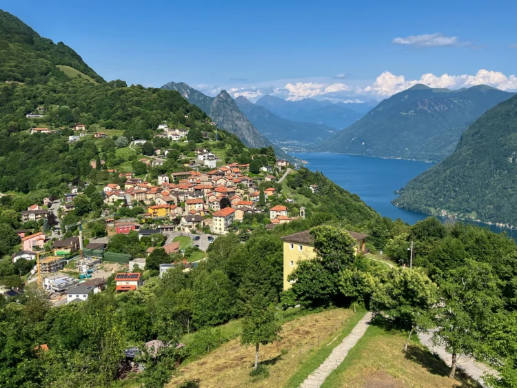 A village with orange roofs tucks into the hillside with the lake and mountains off in the distance.