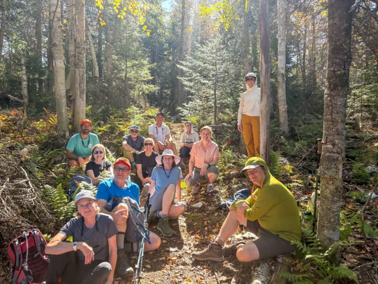 a group of adults pose in a sunny forest. They are all wearing hiking clothes