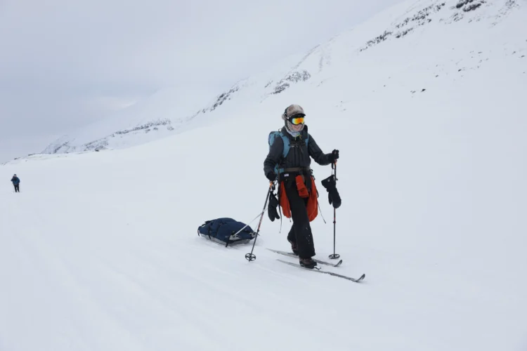Skier glides along with snow with a sled being pulled behind.