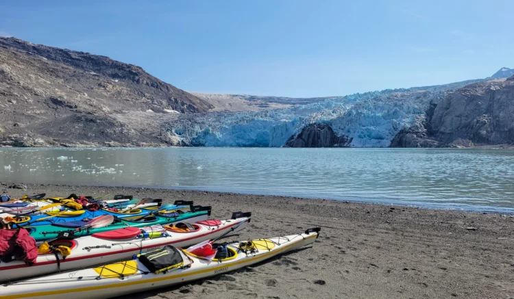 Kayaks line up on the beach with a glacier in the background