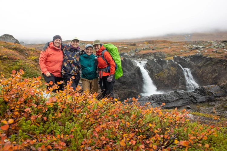 Hikers pose in front of a waterfall and flowers in Sweden