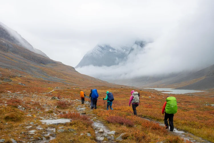 Hikers walk across the tundra with clouds descending behind them in Sweden