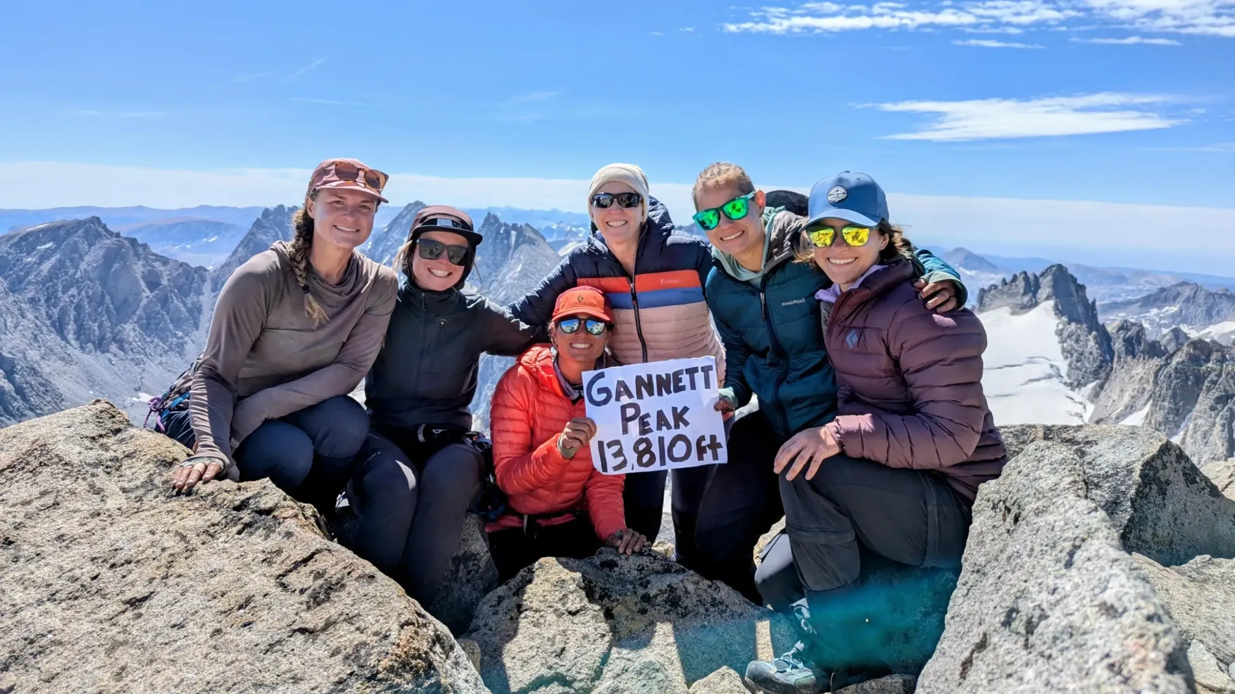 a group of people on a mountain top hold up a sign reading gannett peak 13810 ft.